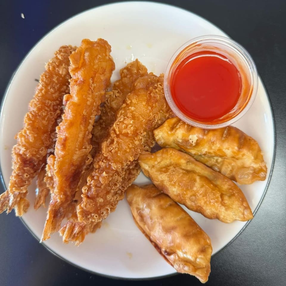Crispy fried shrimp and dumplings with a side of red dipping sauce on a white plate.