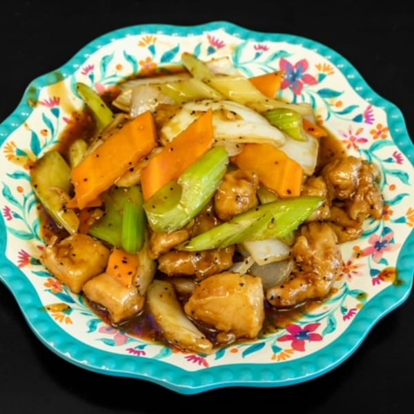Chinese stir-fry with chicken, carrots, celery, and onions in a dark sauce on a floral plate.