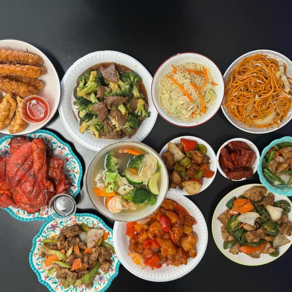An overhead shot of a feast of Chinese dishes, including noodles, beef and broccoli, and sweet and sour chicken.