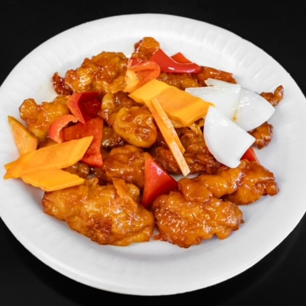 Sweet and sour chicken with red bell peppers, mango, and onions on a white plate.