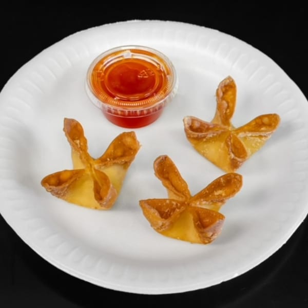 Three golden-brown crab rangoons and a small container of red sweet and sour sauce on a white plate.