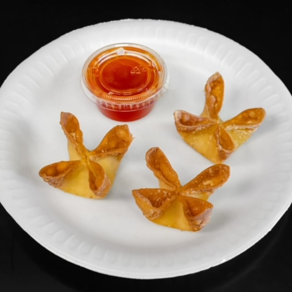 Three golden-brown crab rangoons and a small container of red sweet and sour sauce on a white plate.