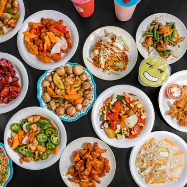 An overhead view of various Chinese dishes, including noodles, stir-fries, and fried appetizers, on a dark surface.