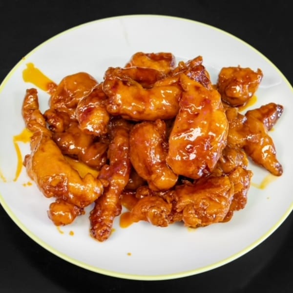A white plate filled with glistening orange chicken pieces, coated in a sweet and savory sauce.