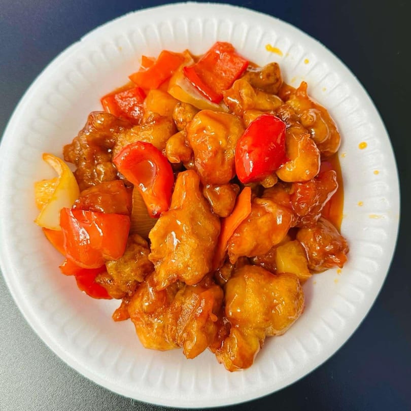 Sweet and sour chicken with red and yellow bell peppers in a white bowl.