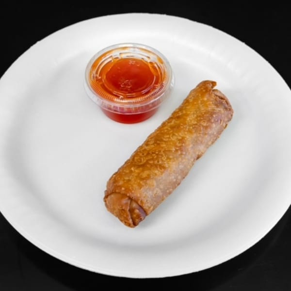 A golden-brown Chinese egg roll and a small plastic cup of sweet and sour sauce on a white plate.