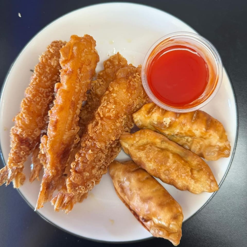 Crispy fried shrimp and dumplings with a side of red dipping sauce on a white plate.