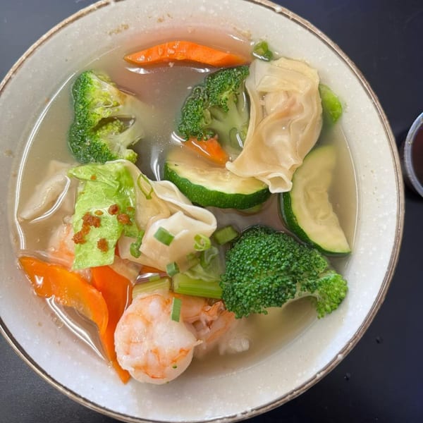 A bowl of Chinese wonton soup with shrimp, broccoli, carrots, zucchini, and green onions.