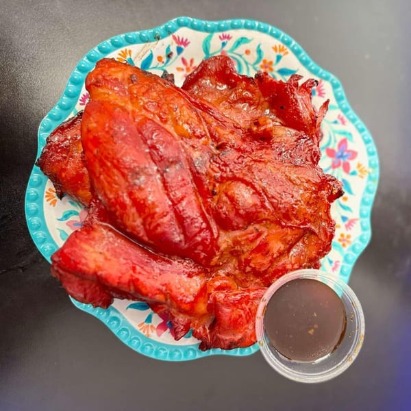 Bright red char siu pork on a floral plate with a side of dark sauce.