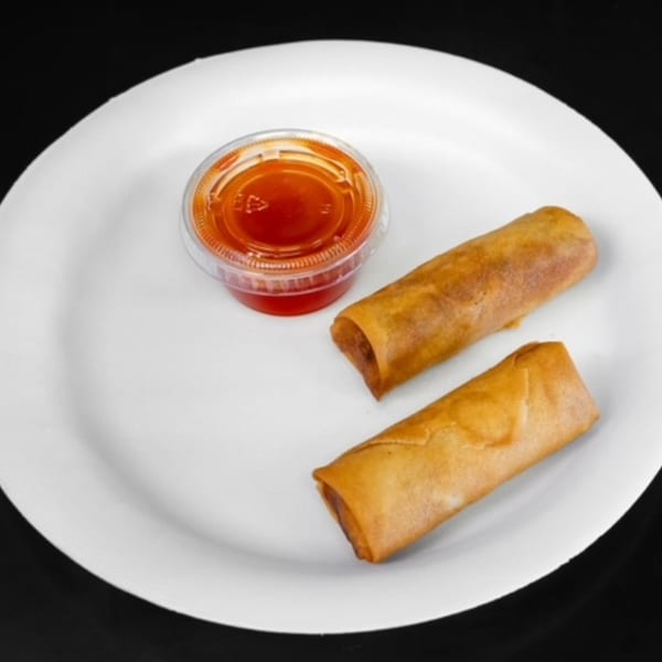 Two golden-brown Chinese egg rolls and a small container of red dipping sauce on a white plate.