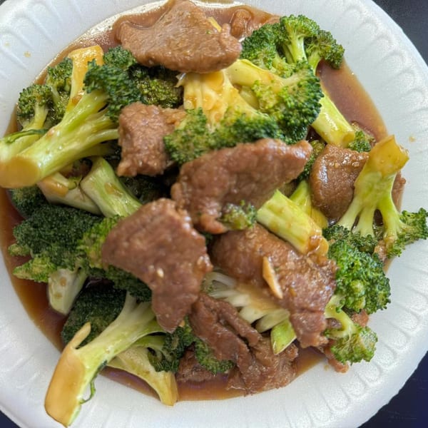 Beef and broccoli in a brown sauce, served on a white styrofoam plate.