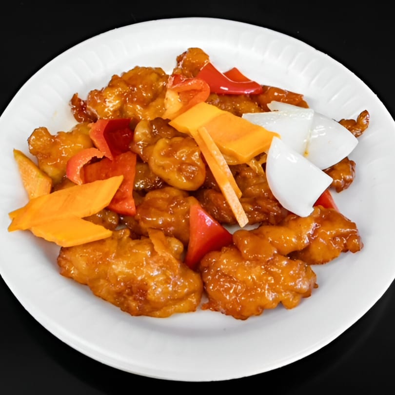 Sweet and sour chicken with red peppers, orange carrots, and white onions on a white plate.